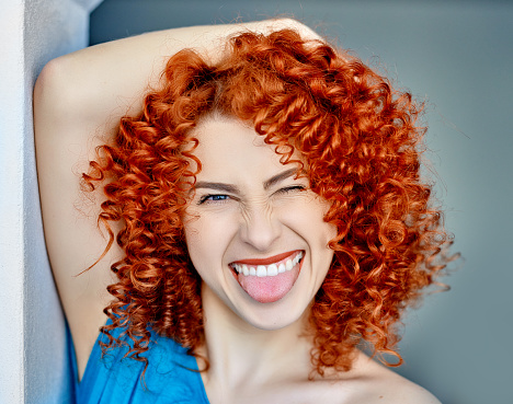 funny woman with red curly hair sticking out tongue and laughing, winking, sweet facial expression.