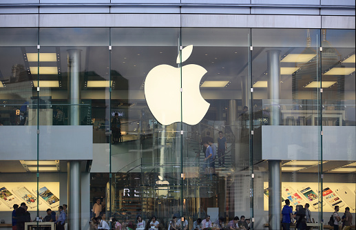 New York, United States - February 11, 2014: Glass building of the Apple Store with huge Apple Logo at 5th Avenue near Central Park. The store is designed as the exterior glass box above the underground display room. There customers waiting on the entrance and a few incidental people seen on the street.
