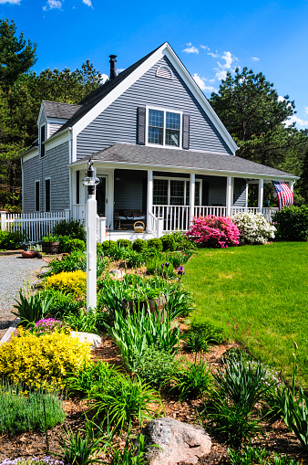 An American flag flies from the open porch and gardens surround a small  single family home on a Spring afternoon on Cape Cod on the Massachusetts coast. (Property release attached)