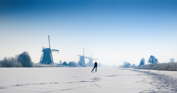 ice-skating man near the traditional windmills at Kinderdijk in snowy landscape at a clear sky in The Netherlands