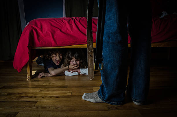 due ragazzi nascosti sotto il letto piangere per paura - under attack foto e immagini stock