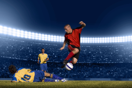 Close up of soccer player feet shooting a ball with powerful toward a goal while playing on a stadium with crowds spectators background