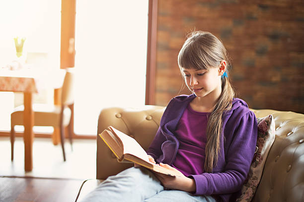 istock Little girl reading a book on the couch. 474920340