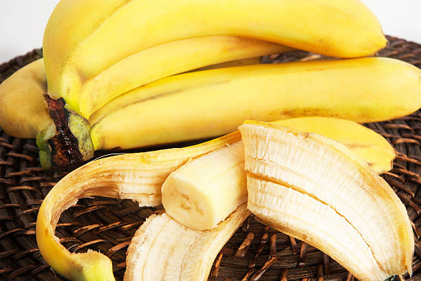 букет бананов и один очищенного банана. - banana bunch yellow healthy lifestyle стоковые фото и изображения