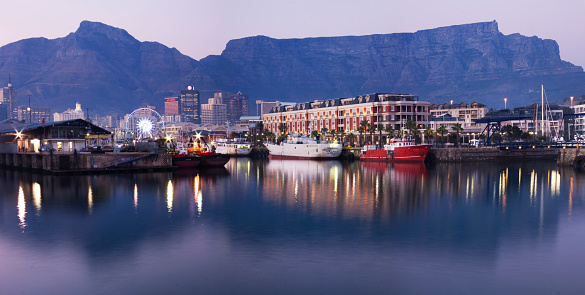 A photograph of the Water Front in Cape Town, South Africa tanken in the evening. With Table Mountain in the background and the waterfront lights reflecting in the harbour water in the forground