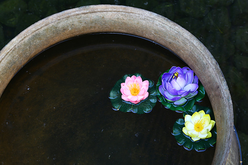 Vietnamese pot full of water and multi colored flowers floating.