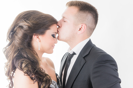 Studio isolated portrait of newly engaged couple, where the guy kissing the forehead of the woman.