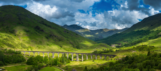Summer sunlight illuminating the iconic arches of the Gelnfinnan Viaduct as it curves across the green glen at the end of Loch Shiel overlooked by the rugged mountain peaks of the Highlands, Scotland. ProPhoto RGB profile for maximum color fidelity and gamut.