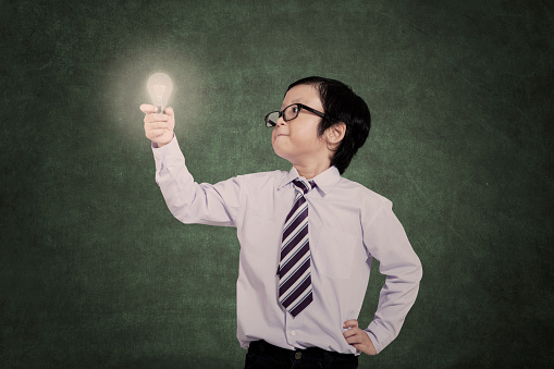 Confident little businessman looking at lit bulb in class