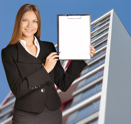 Business woman standing on background building, and indicates ballpoint pen in the clipboard.