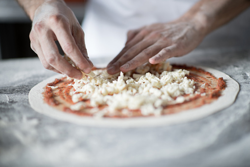 Close up of a person making pizza at an Italian restaurant and putting cheese on the dough