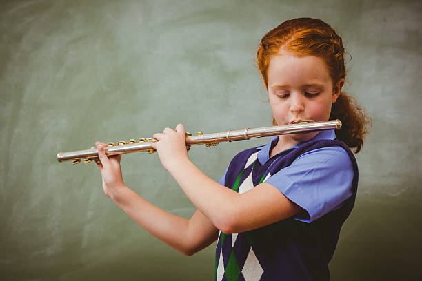 istock Cute little girl playing flute in classroom 474963150