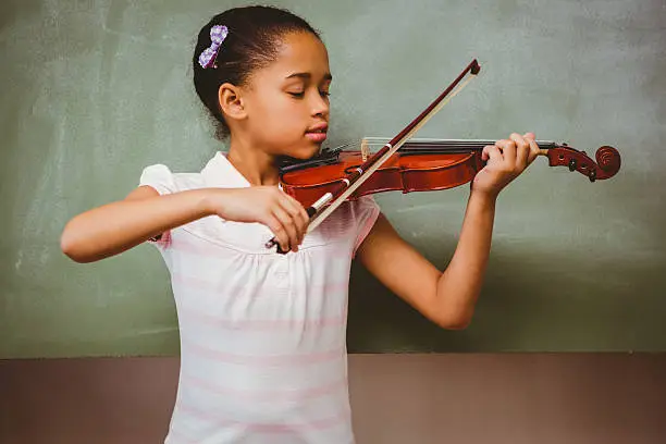 Portrait of cute little girl playing violin in classroom