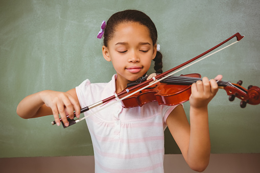 Portrait of cute little girl playing violin in classroom