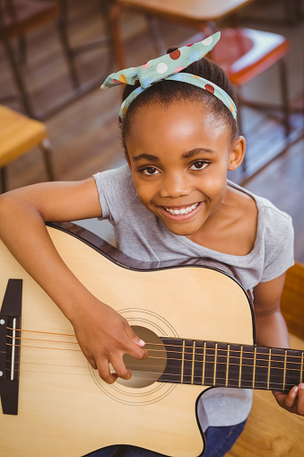 Portrait of cute little girl playing guitar in classroom