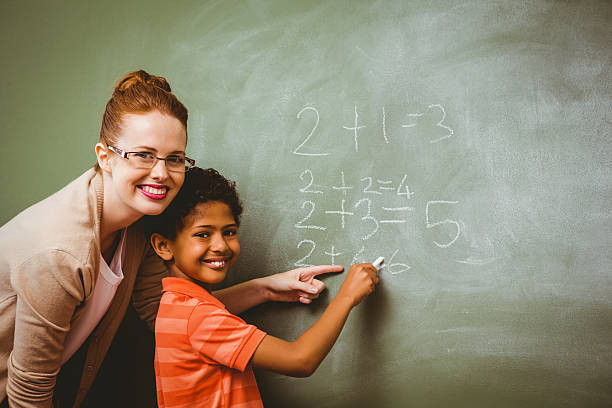 istock Teacher assisting boy to write on blackboard in classroom 474964862