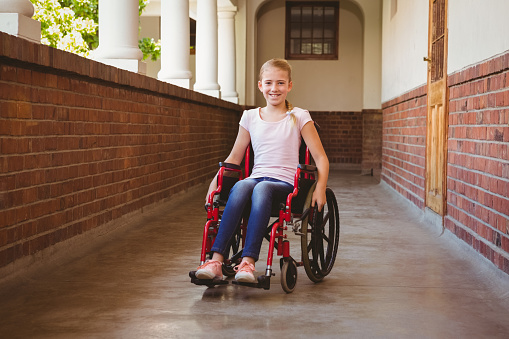 Portrait of cute little girl sitting in wheelchair in school corridor