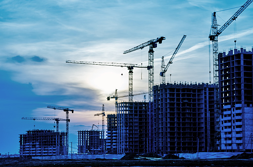 Construction site at dusk evening back light, silhouette crane, sun, toned in blue