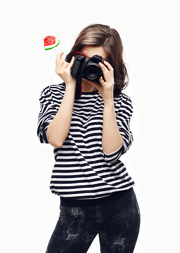 Portrait of pretty girl,holding a watermelon  candy,wearing striped top, looking at camera.Blue background