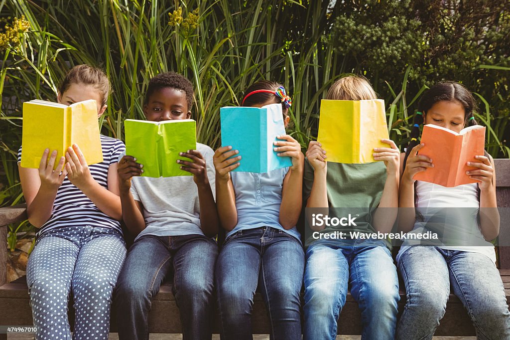 Children reading books at park Children sitting in row and reading books at the park Child Stock Photo
