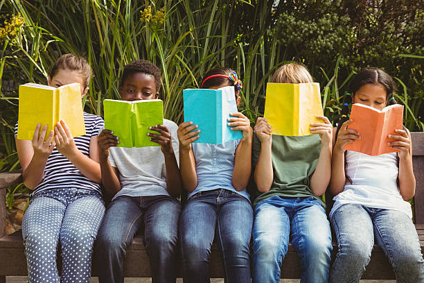 Children reading books at park Children sitting in row and reading books at the park children reading images stock pictures, royalty-free photos & images