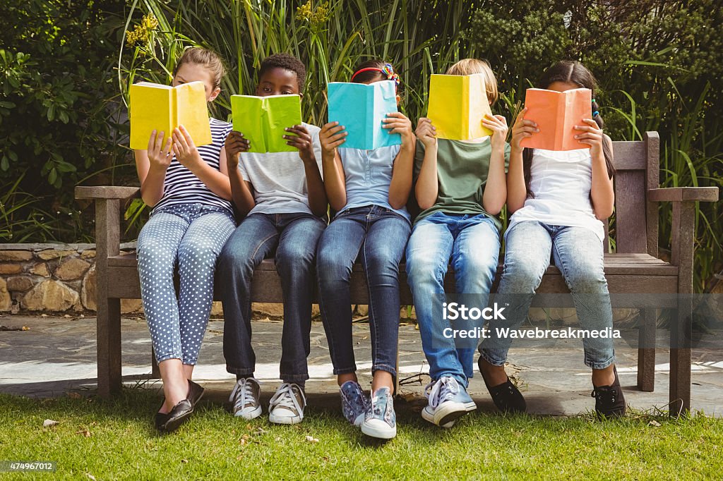 Children reading books at park Children sitting in row and reading books at the park Reading Stock Photo