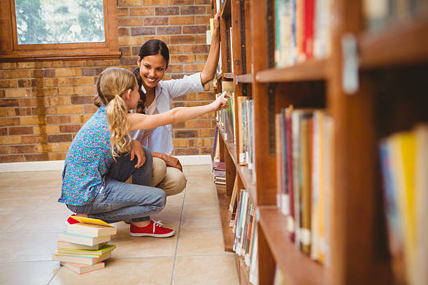 istock Teacher and little girl selecting book in library 474967102