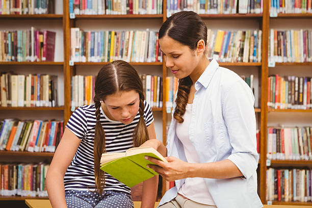 istock Teacher and girl reading book in library 474967168