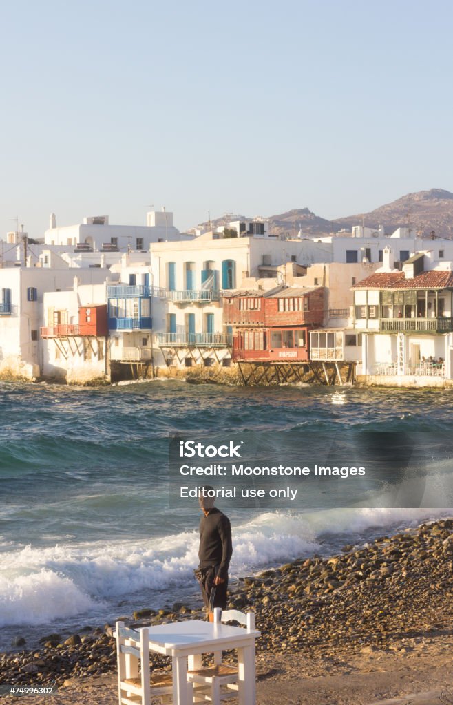 Little Venice in Mykonos Town, Greece Mykonos Town, Greece - August 30, 2014: A Caucasian man stands in front of Little Venice waterfront in Mykonos with waves crashing in the background. 20-24 Years Stock Photo