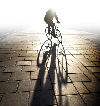 Back lit cyclist in evening light casting long shadow on sidewalk