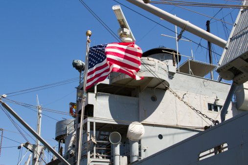An American flag waves proudly atop an American Navy ship. American pride and dedication for the armed forces. Patriotism for the American flag.