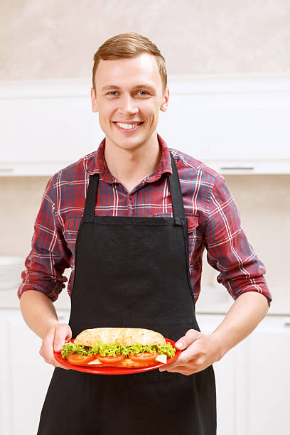 istock Smiling man holding plate with big sandwich on 475005822