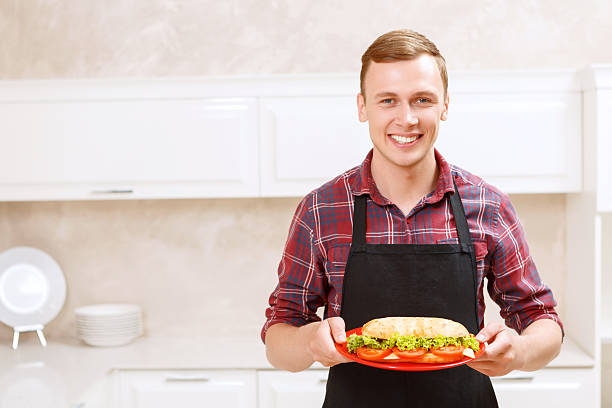 istock Smiling man holding plate with big sandwich on 475005846
