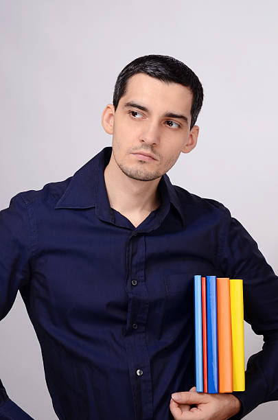 istock Student holding a pile of books under arm looking away. 475033375