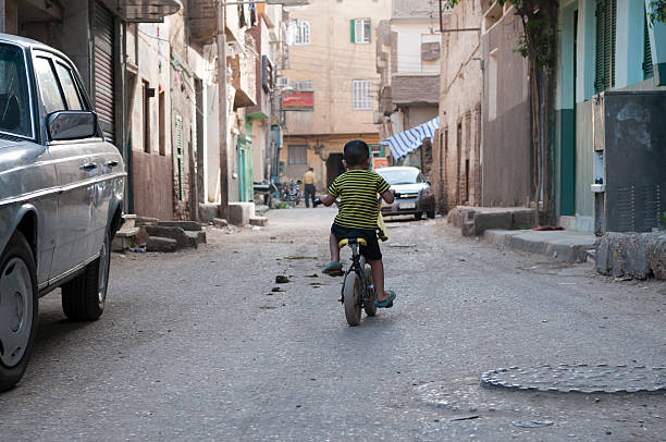 A two children riding bicycles on quiet street, surrounded by greenery and houses, enjoying sunny day. their bright shirts add cheerful touch to scene