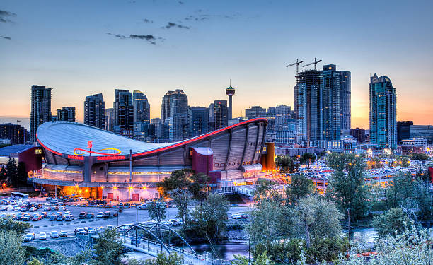 Sunset Over Downtown Calgary and Saddledome Calgary, Canada - May 23, 2015: Sunset over Calgary's skyline with the Scotiabank Saddledome in the foreground. The dome with its unique saddle shape is home to the Calgary Flames NHL club, and is one of the oldest professional hockey arenas in North America. scotiabank saddledome stock pictures, royalty-free photos & images