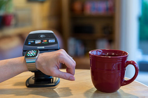 Woman Paying using Apple Watch and Electronic Reader Montreal, Сanada - May 25, 2015: Woman Paying at a coffee shop counter using Apple Watch and an electronic reader. The Apple Watch became available April 24, 2015 and is the latest device produced by Apple. american express stock pictures, royalty-free photos & images