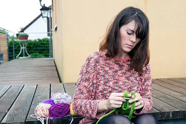 young woman sitting outdoors and is knitting