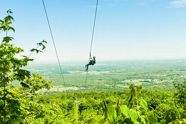 Young woman zip-lining with aerial countryside view at Blue Mountain, Ontario, Canada.