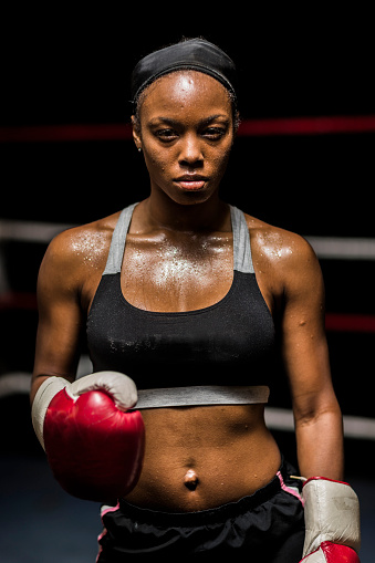 Young woman boxer holding up red boxing gloves ready to box in a boxing ring.