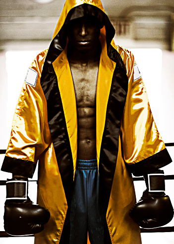 Young male boxer with boxing gloves and boxing robe waiting in boxing ring.