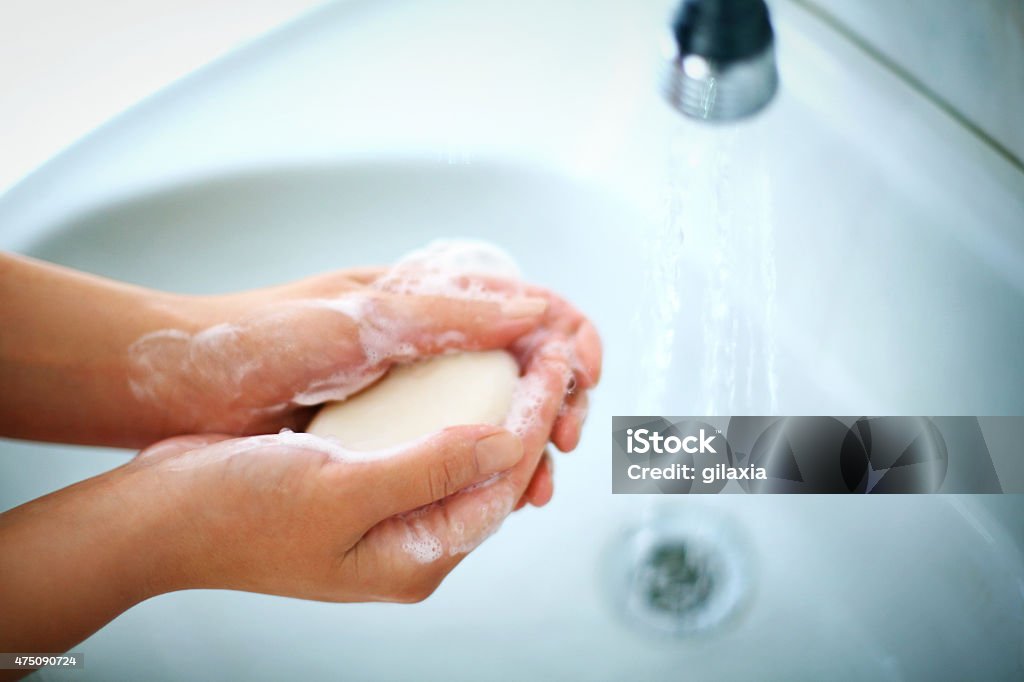 Woman washing her hands. Top view of unrecognizable caucasian woman washing her hands with soap in bathroom. Water is pouring over her hands, visible bluish sink in background. Blue Stock Photo