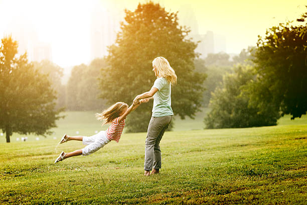 Mother holding daughters hand while spinning her around and around in the park.