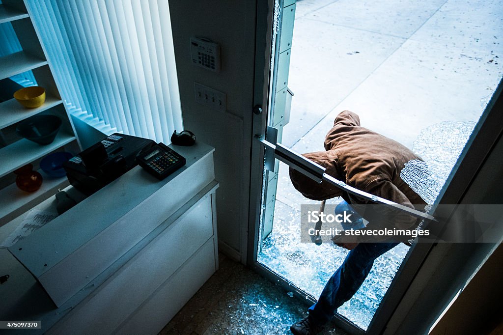 Robber using a sledgehammer, A robber using a sledgehammer to break the glass of a retail store. Thief Stock Photo