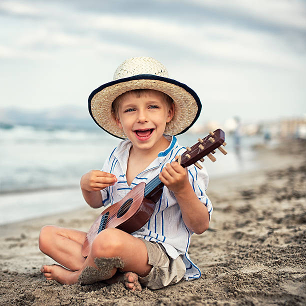 istock Little boy playing ukulele on the beach. 475114434