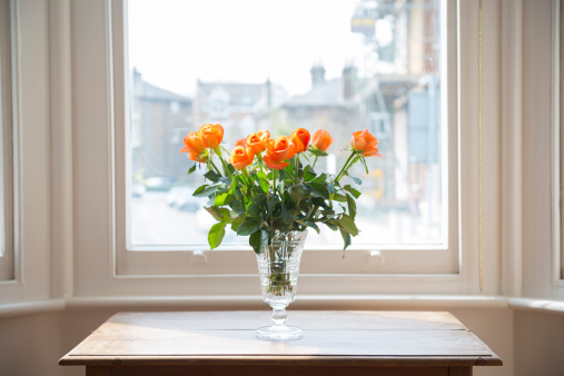 Vase of flowers on a table by a window. Orange tea roses.