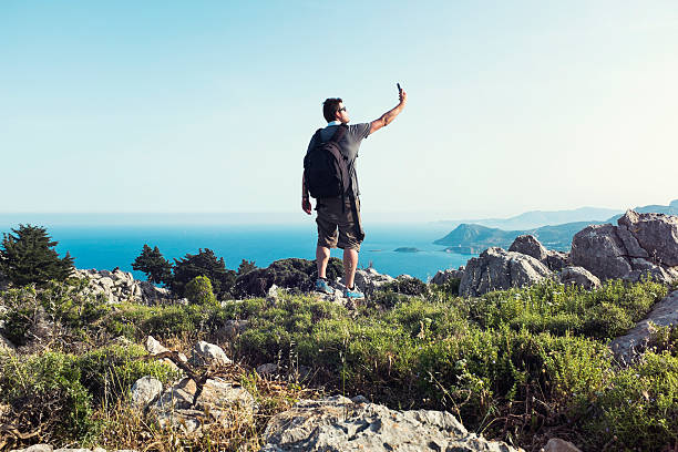 rucksacktourist schießt selfie während auf mountain top - behind photographer men mountain climbing stock-fotos und bilder