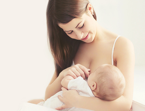Soft photo young mother feeding breast her baby at home in white room