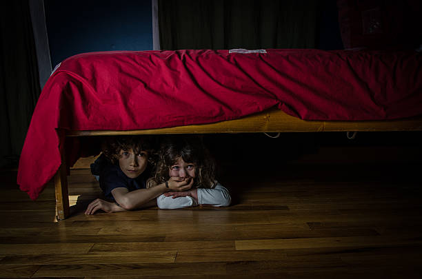 bambini nascosti sotto il letto con la paura e piangere - under attack foto e immagini stock