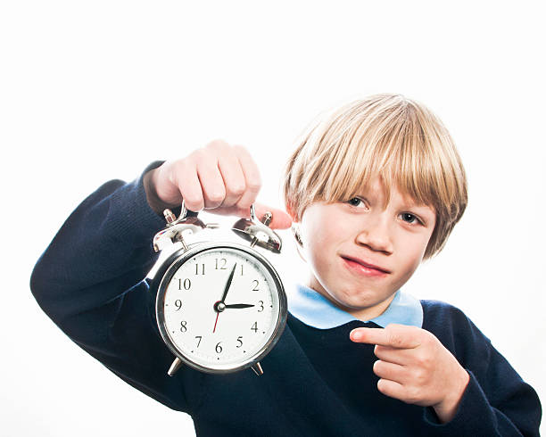 istock School boy holding a clock and pointing at the time 475143890